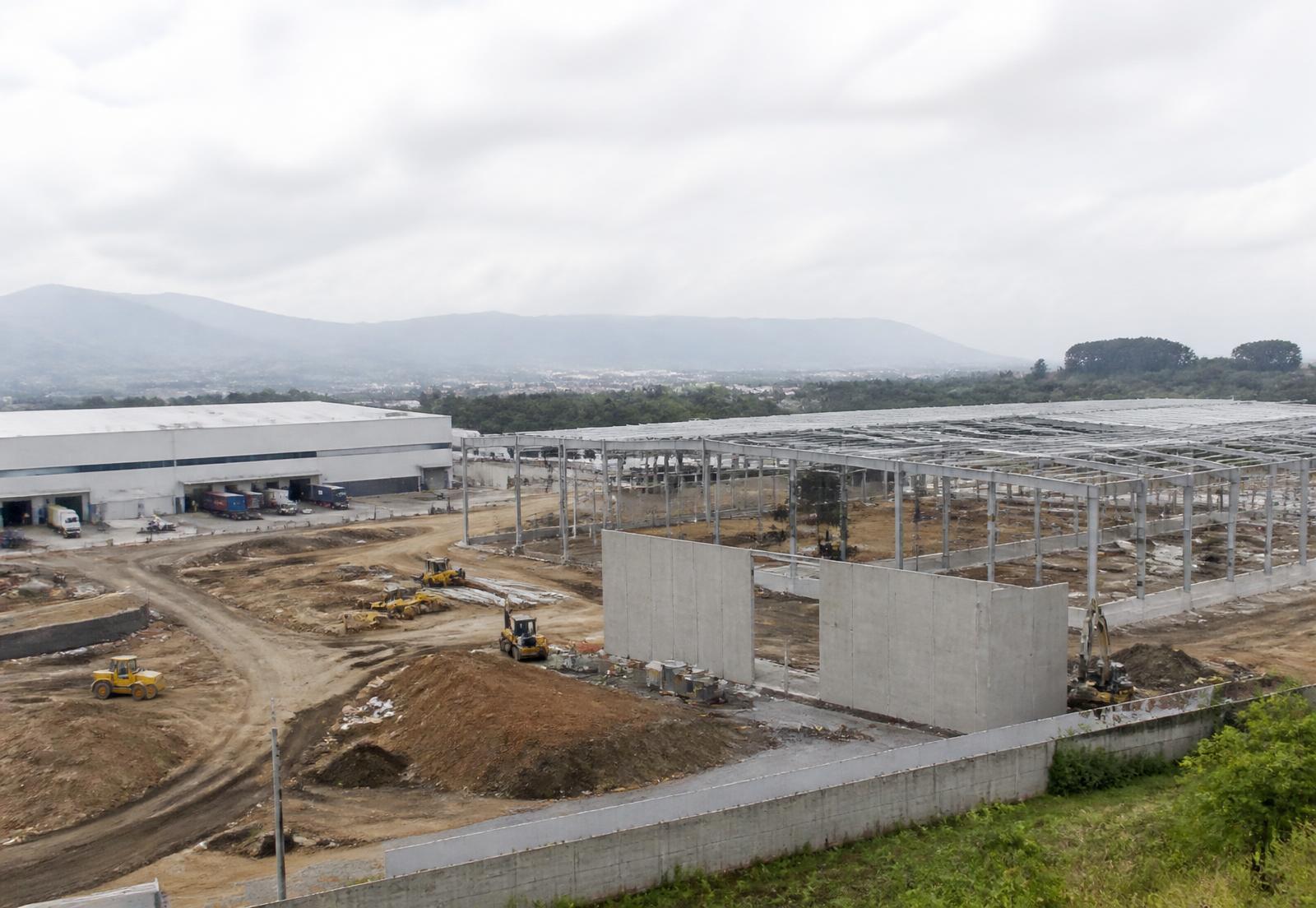Parque industrial y logístico en construcción en Guatemala, con naves de estructura metálica y maquinaria de movimiento de tierras