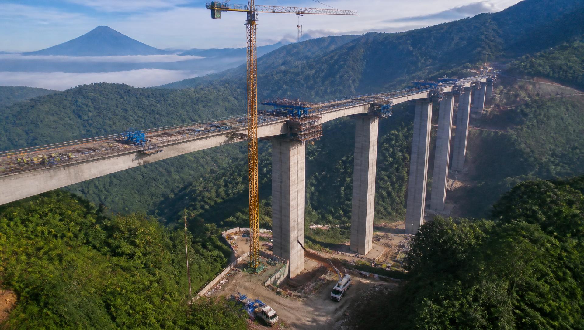 Viaducto de carretera en construcción sobre un valle del altiplano guatemalteco, con pilas de hormigón, vigas prefabricadas y grúas